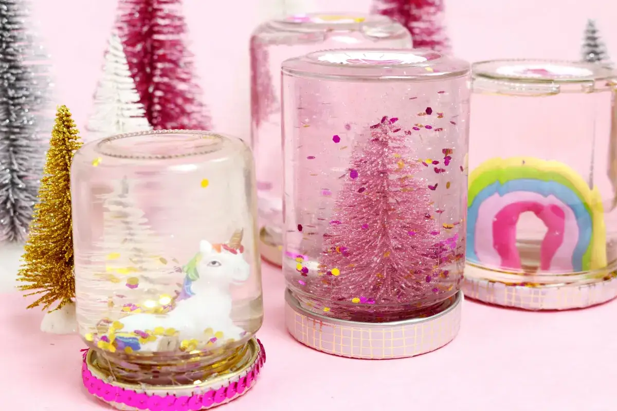 Zauberhafte Schneekugeln selber machen: Ein Einhorn, ein rosa Tannenbaum und ein Regenbogen in Gl&auml;sern mit Glitzer.