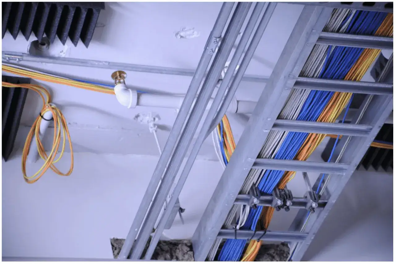 Instalaci&oacute;n de cables lszh de colores (azul, naranja, amarillo, blanco) en una bandeja met&aacute;lica, junto a tuber&iacute;as y un rociador.