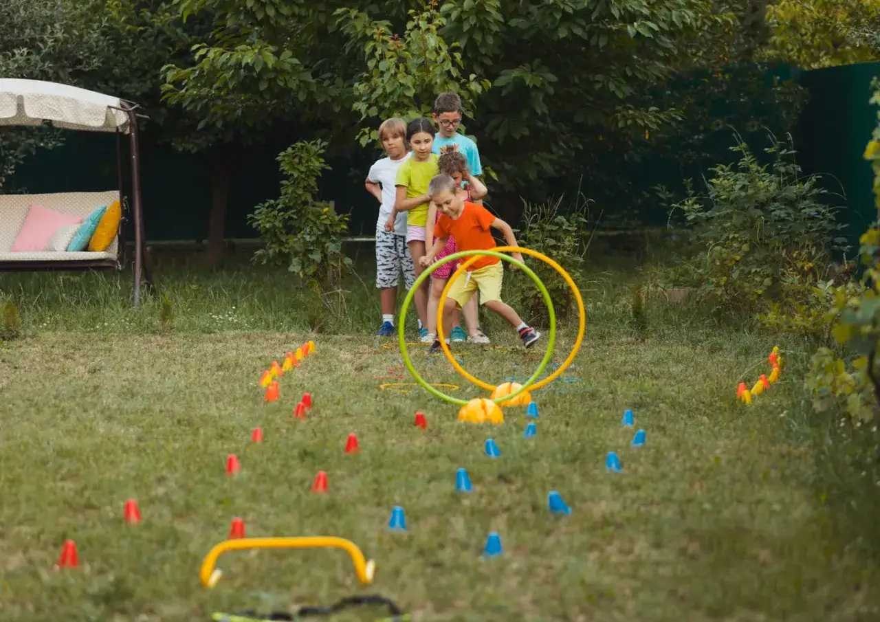 Bambini si divertono con giochi da fare in giardino: corrono tra coni colorati e cerchi, pronti per una gara di agilità.