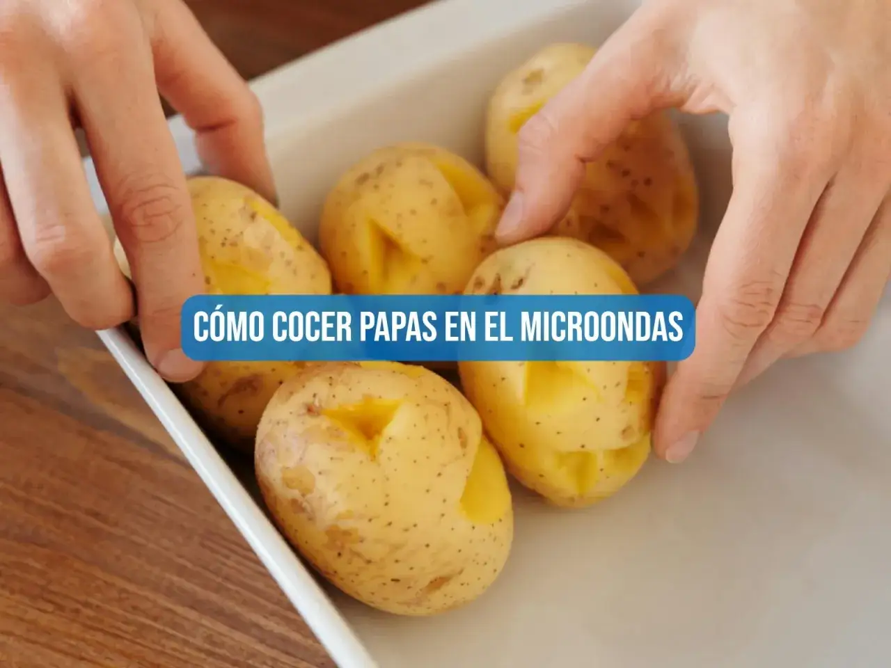 Manos colocando papas con cortes en una bandeja blanca para cocerlas al microondas.