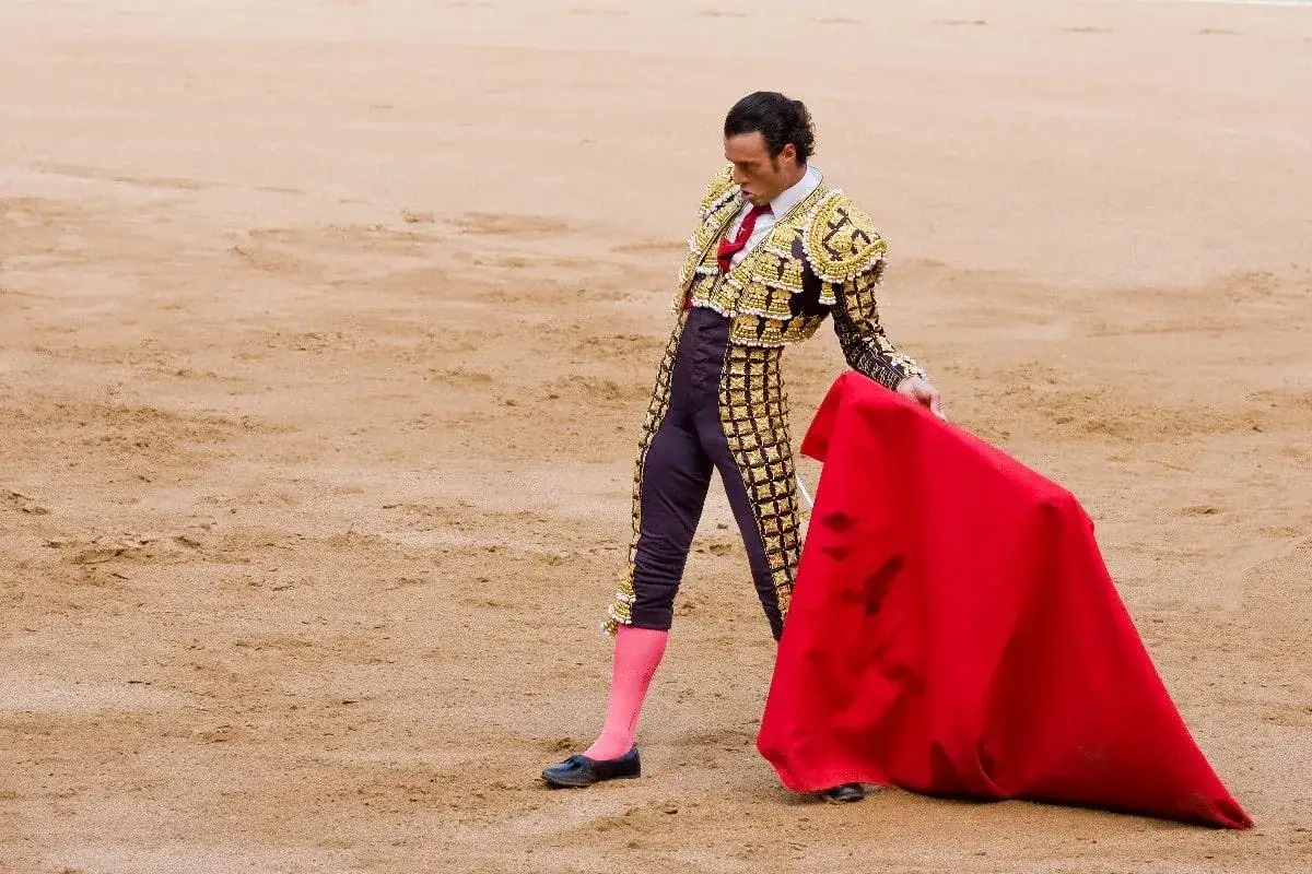 Un torero con traje de luces dorado y negro, medias rosas y capote rojo, evoca la imagen de los toreros de los 90.