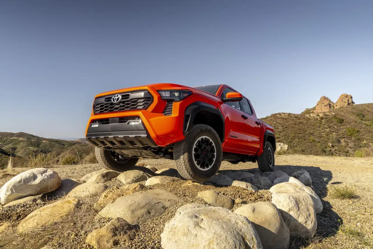 Pomarańczowy Toyota pickup pokonuje kamienisty teren.