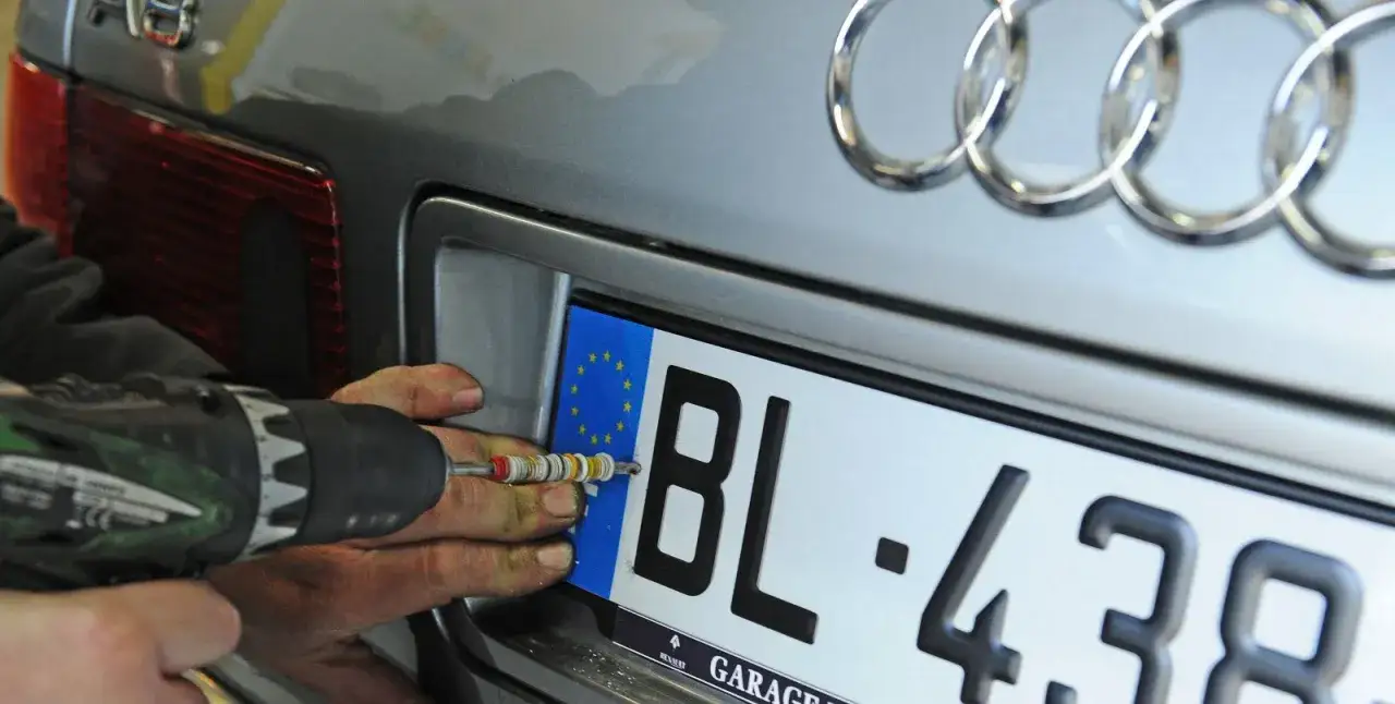 Une personne utilise une perceuse pour fixer une plaque d'immatriculation. Que faire en cas de vol de plaque d'immatriculation ?