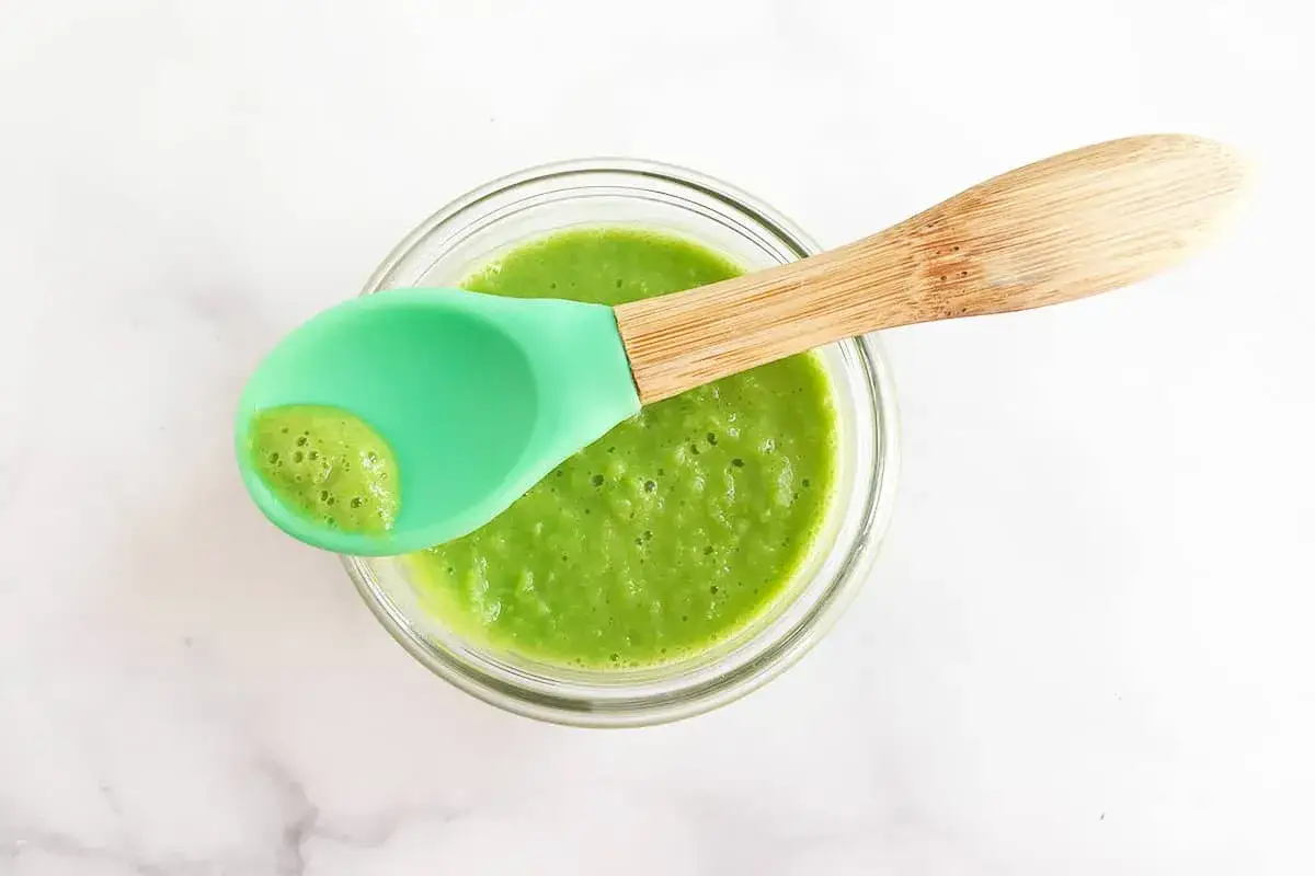 Un taz&oacute;n de pur&eacute; de guisantes para beb&eacute;, con una cuchara verde de silicona lista para alimentar.