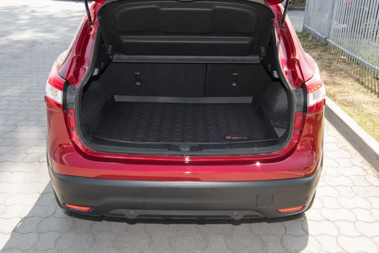 Czerwony Nissan Qashqai J11 z otwartym bagażnikiem, w którym widać czarną, gumową matę z wytłoczonym wzorem.