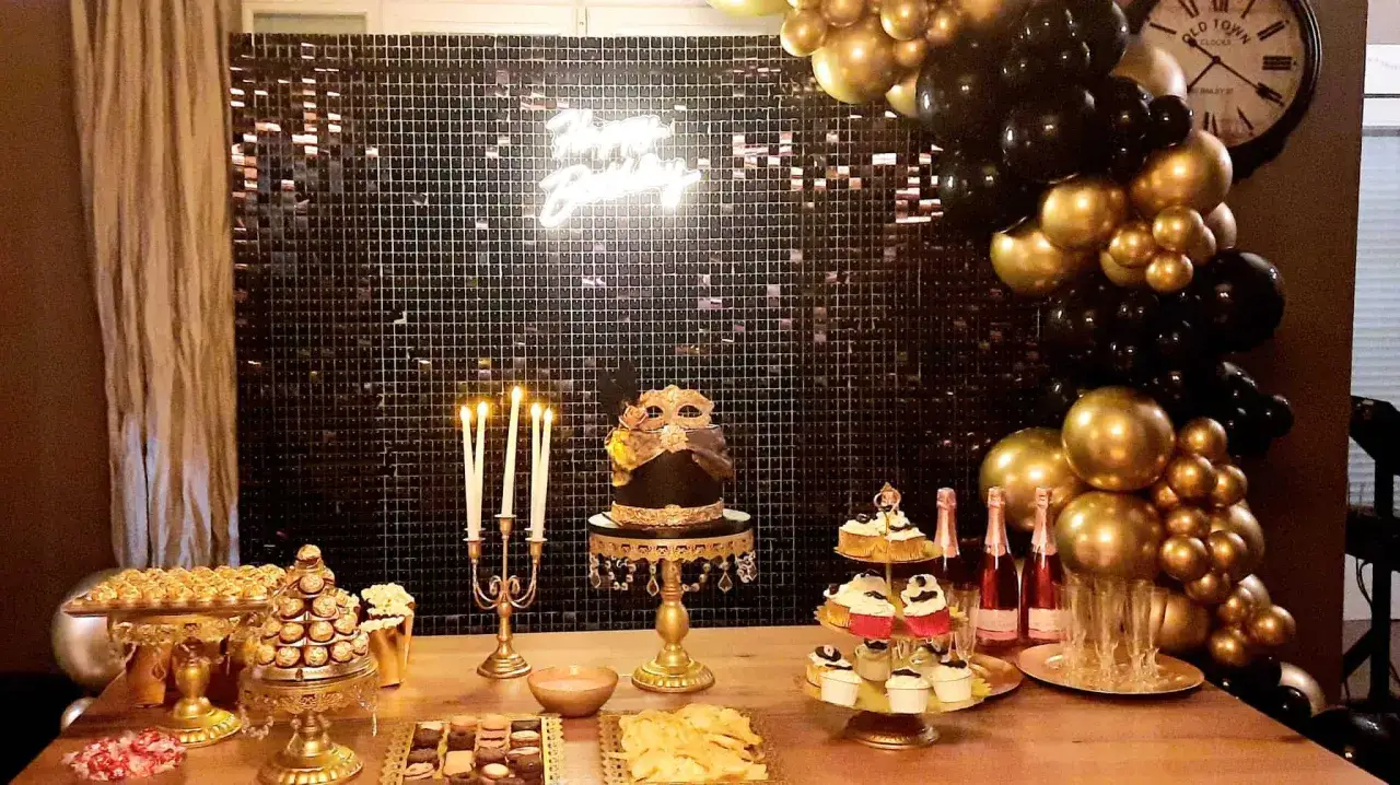 Mesa de dulces para **fiesta cumplea&ntilde;os adultos divertidas** con pastel tem&aacute;tico, cupcakes, chocolates y globos dorados y negros.