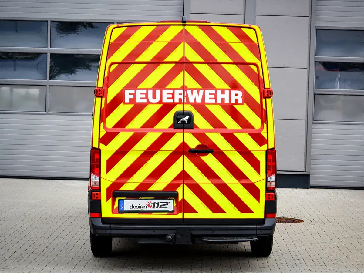 Feuerwehr-Transporter mit auffälliger Warnbeklebung nach DIN 14502-3. Rot-gelbe Diagonalstreifen sorgen für hohe Sichtbarkeit.