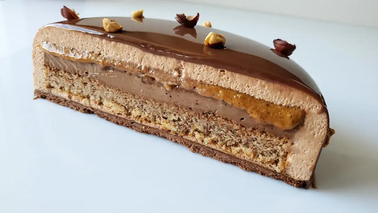 Tranche d'un tiramisu noisette aux couches de mousse chocolat, caramel et biscuit croustillant, d&eacute;cor&eacute; de noisettes enti&egrave;res.
