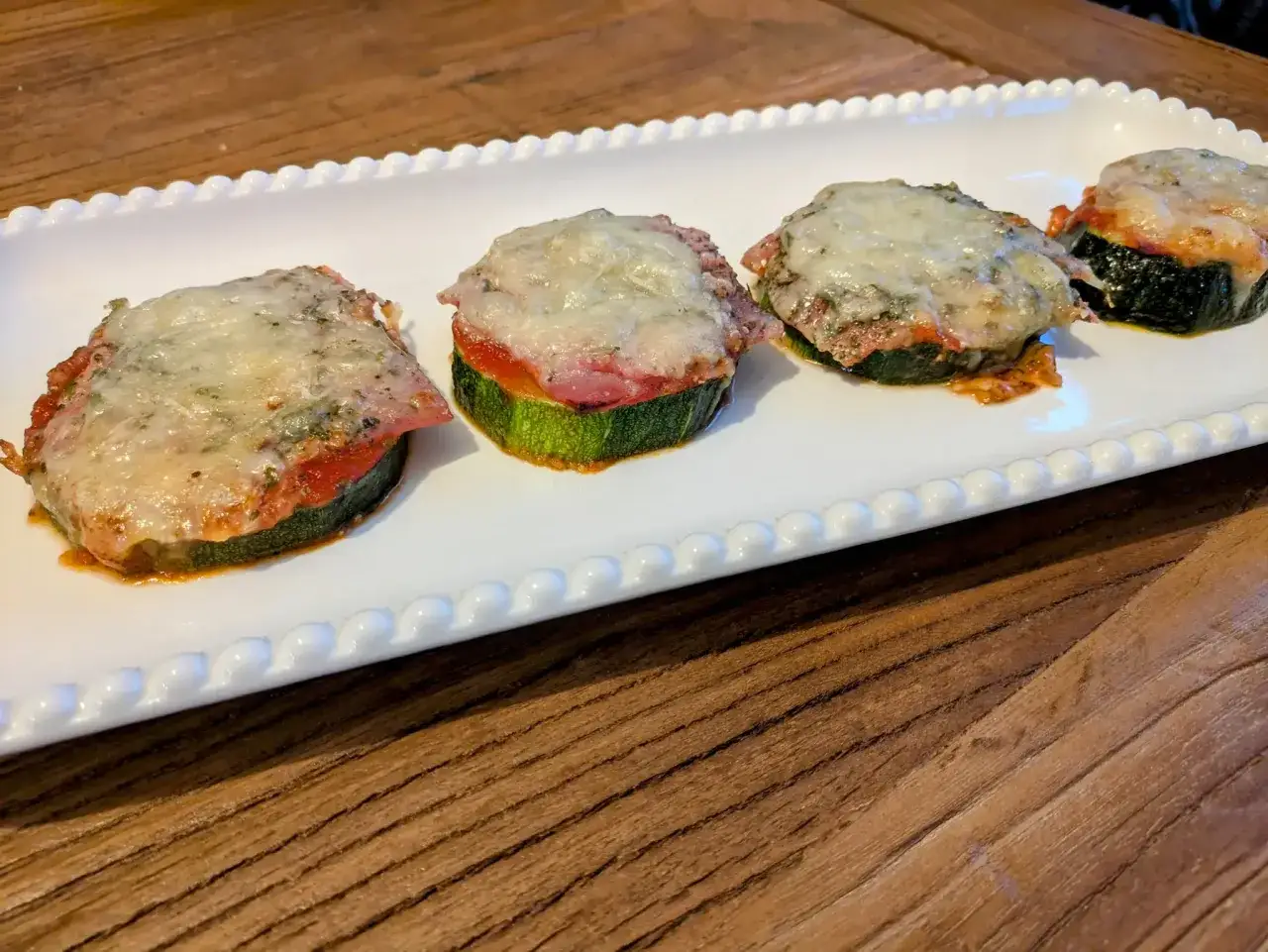 Quatre rondelles de courgette fa&ccedil;on pizza, garnies de sauce tomate, jambon et fromage fondu, servies sur un plat blanc.