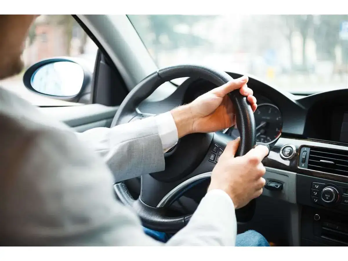 Mani salde sul volante, un uomo con giacca grigia guida con sicurezza. La sua postura suggerisce una guida esperta, pronto ad affrontare ogni curva.