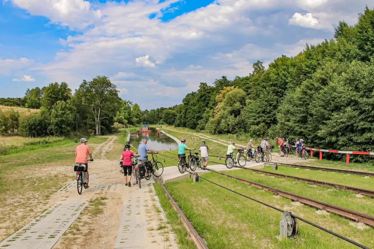Grupa rowerzystów przemierza malowniczy szlak kanału elbląskiego, podziwiając przyrodę i zabytkowe pochylnie.