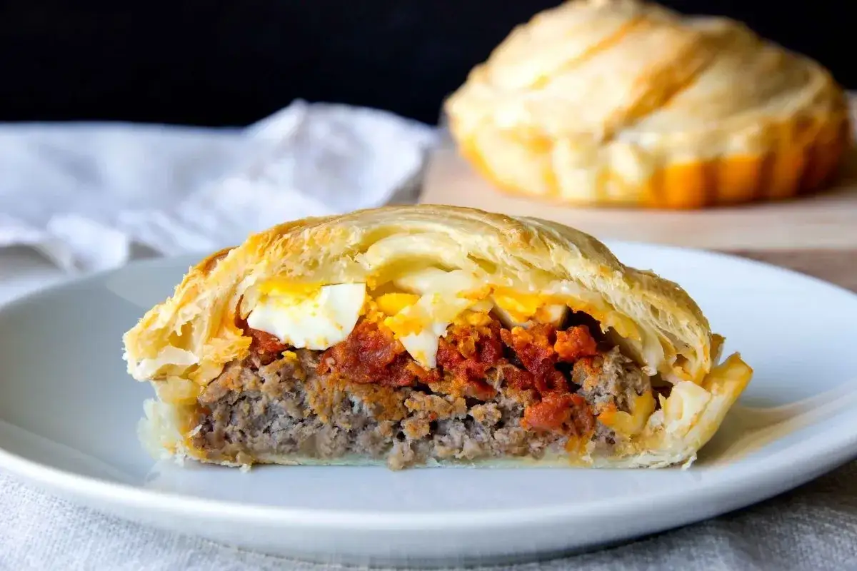 Un corte de pan de carne jugoso, relleno de carne molida, salsa de tomate y huevo duro, envuelto en masa dorada.