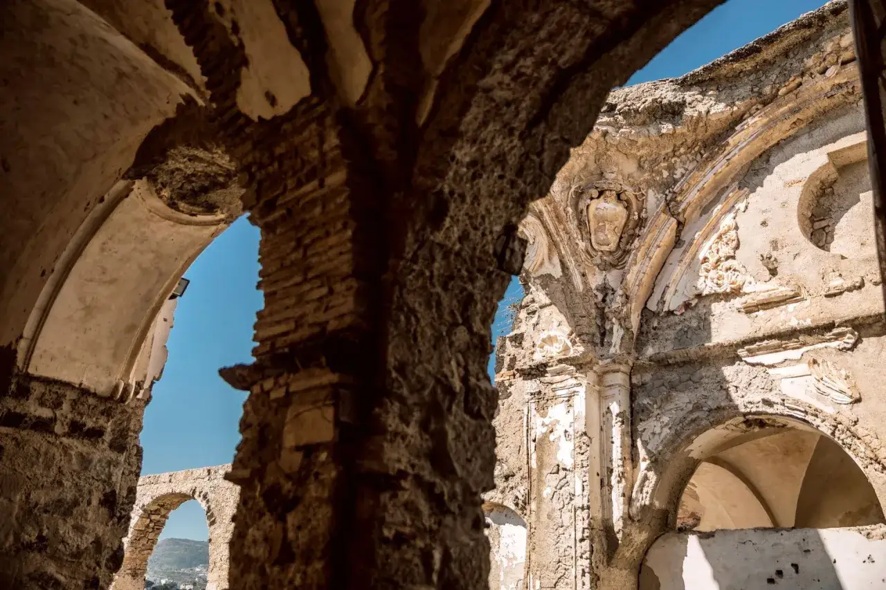 Interni del Castello Aragonese di Ischia: rovine suggestive con archi in pietra e dettagli architettonici antichi, tra cui uno stemma nobiliare.