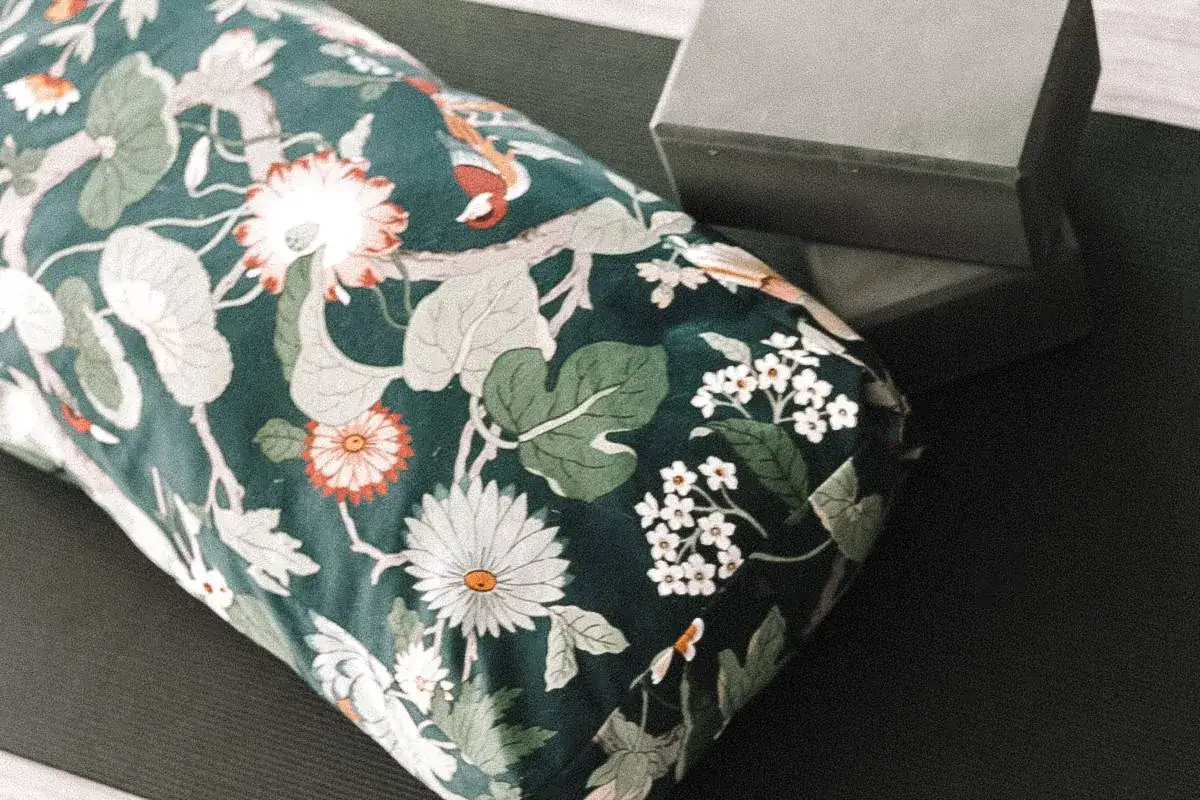 Blumengemustertes Yogakissen auf schwarzer Matte, daneben ein grauer Yogablock. Perfekt f&uuml;r dein DIY-Projekt: schnittmuster yogakissen kostenlos.