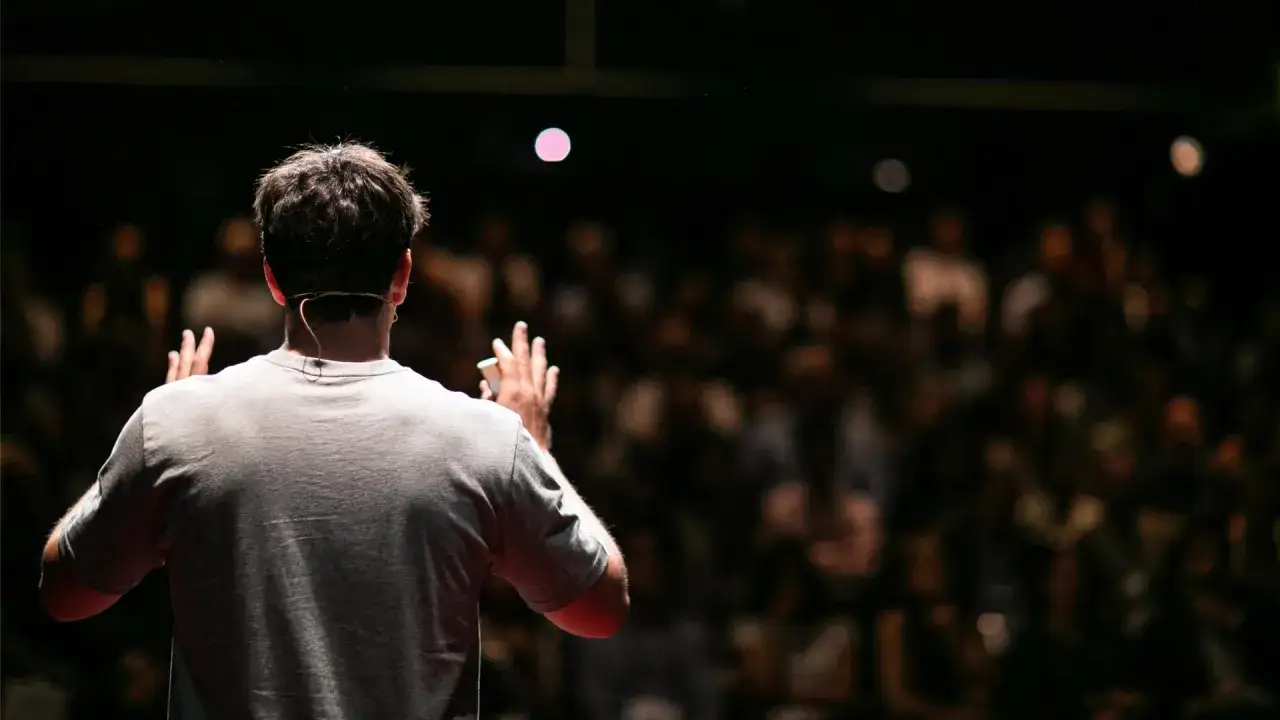 Un relatore, con un microfono dietro l'orecchio, si rivolge a un pubblico numeroso. È il momento del suo breve discorso di saluto.