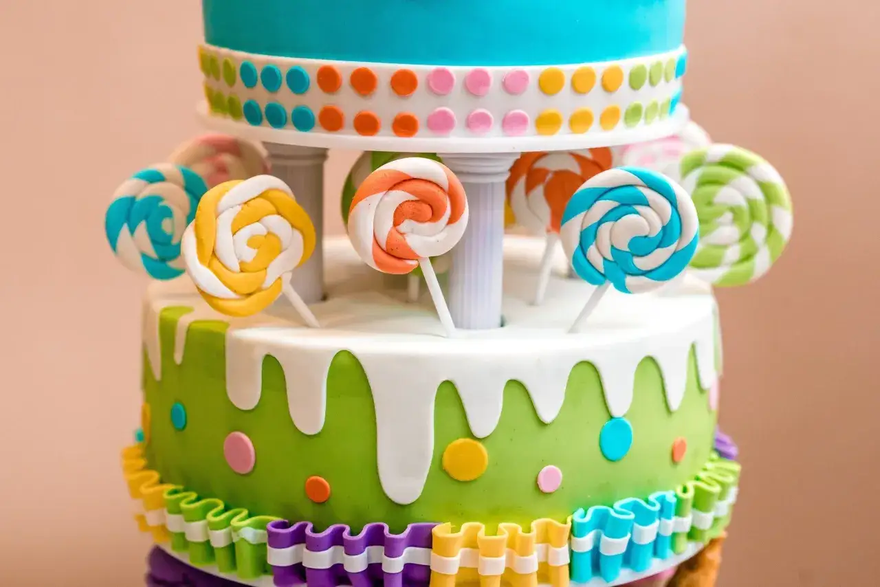Gâteau à plusieurs étages décoré de sucettes colorées en pâte à sucre, de pois et de volants.