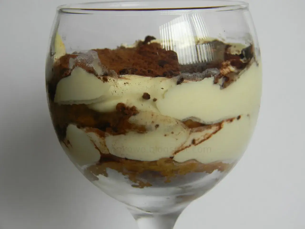 Warstwowe tiramisu bez alkoholu w kieliszku, przełożone kremem i biszkoptami, posypane kakao.