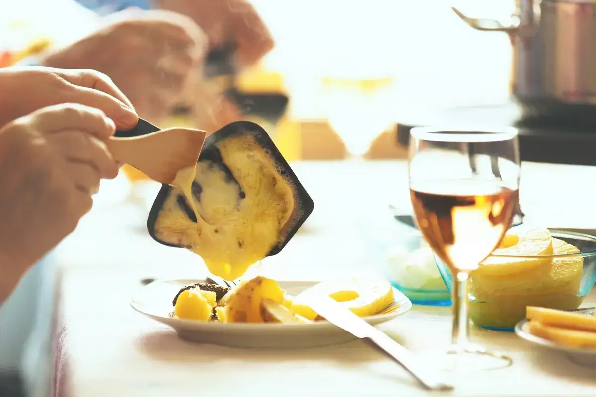 Un verre de vin blanc ou rosé accompagne parfaitement la raclette. On voit du fromage fondu versé sur des pommes de terre.