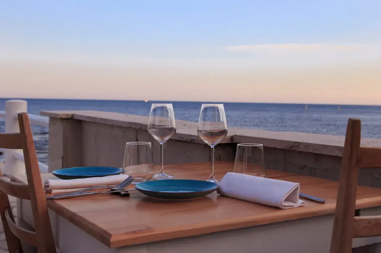 Un tavolo apparecchiato con piatti blu, bicchieri e tovaglioli bianchi, pronto per un **capriccio mattinata** vista mare.