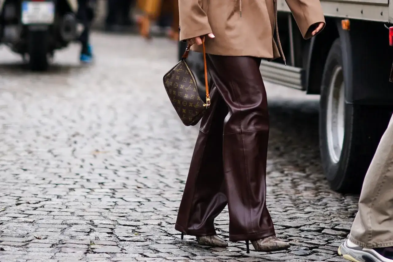 Elegancka stylizacja: brązowe skórzane spodnie, beżowa marynarka i torebka Louis Vuitton. Idealna inspiracja, co ubrać do skórzanych spodni.