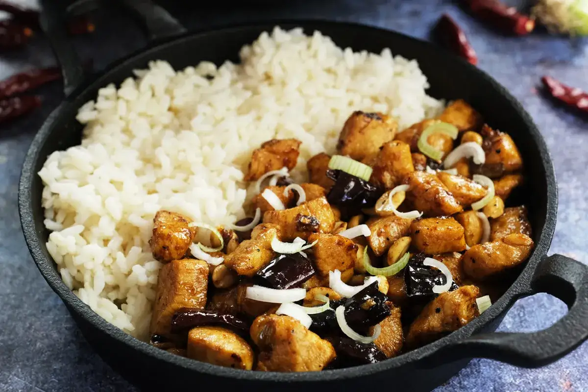 Pyszny kurczak kung pao z ryżem, orzeszkami ziemnymi i szczypiorkiem w żeliwnej patelni.