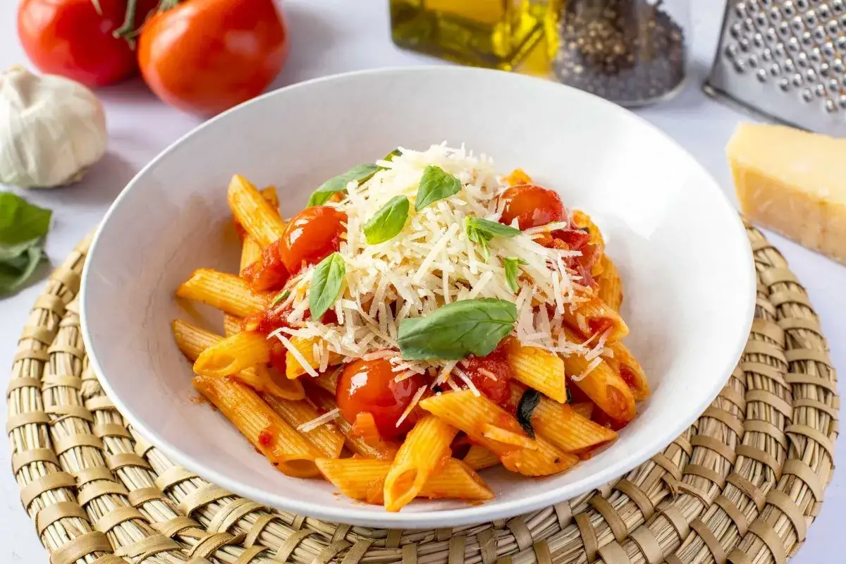 Macarrones con tomate, cubiertos de queso rallado y hojas de albahaca fresca. Un plato sencillo y delicioso.