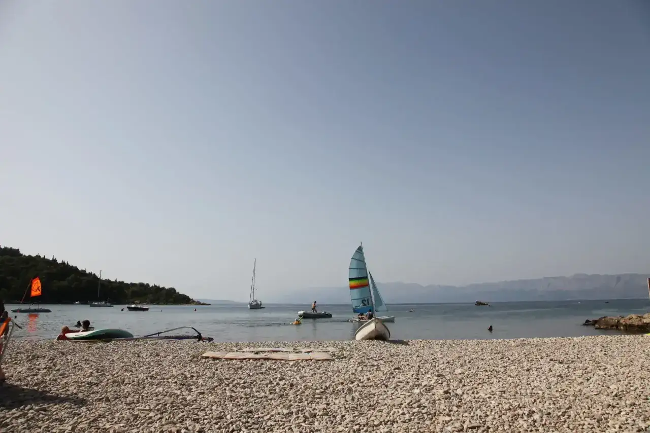 Plaża w campingu Vrila z łódkami, żaglówkami i ludźmi cieszącymi się słońcem i wodą.