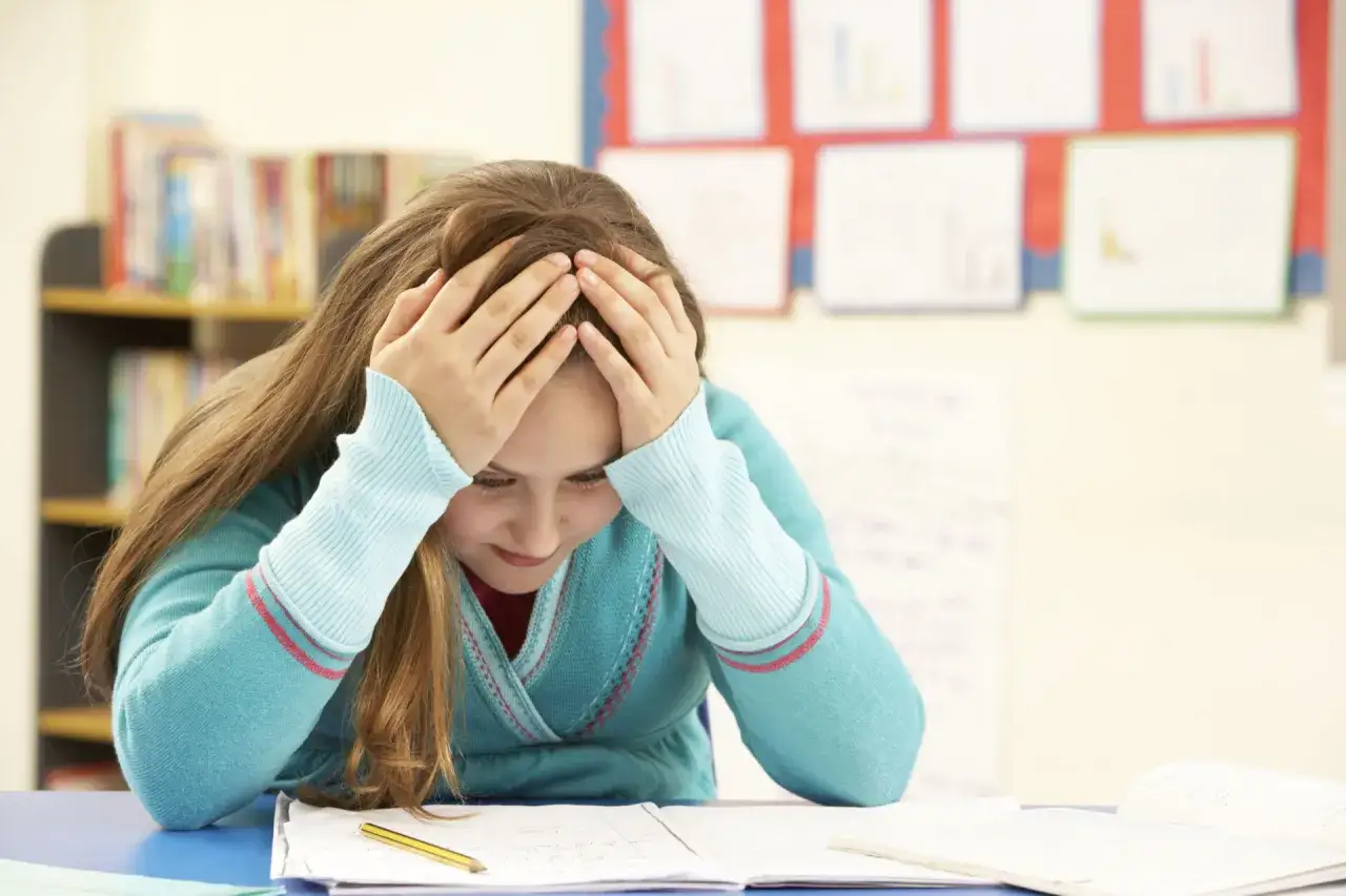 Mädchen mit Händen am Kopf, frustriert über Schulaufgaben. Vielleicht eine **Kollektivstrafe Schule**?
