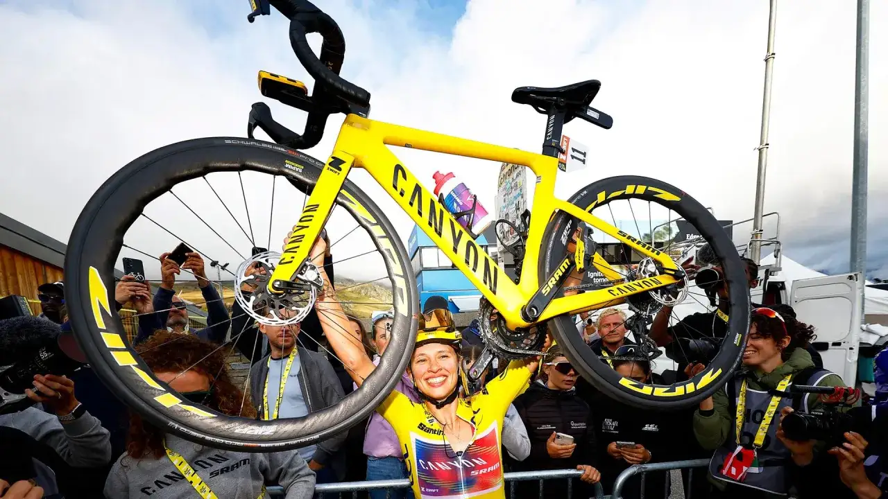 Kasia Niewiadoma jubelt mit ihrem gelben Canyon-Rennrad über dem Kopf, umgeben von Fans und Kameras.