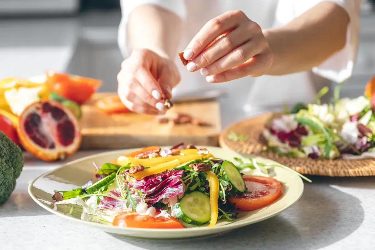 Manos a&ntilde;aden nueces a una ensalada colorida, parte de una dieta antiinflamatoria para la menopausia.