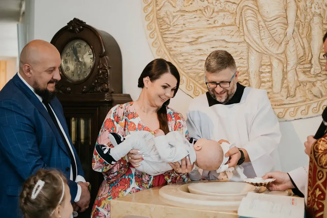 Wzruszająca chwila, kiedy chrzci się dzieci. Rodzice z dumą trzymają niemowlę, a ksiądz przygotowuje się do obrzędu.