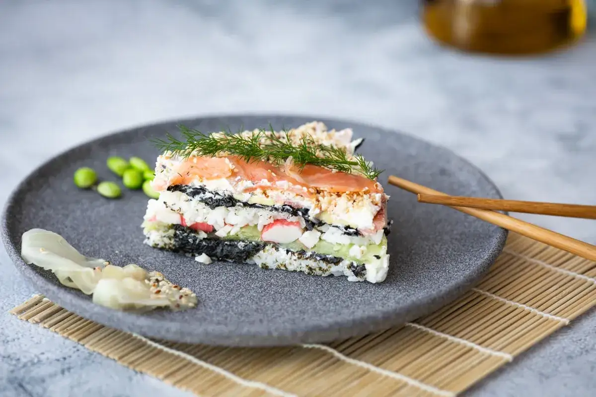 En bit av en vacker sushi tårta med lax, ris, alger och grönsaker. Serveras med edamamebönor och ingefära.