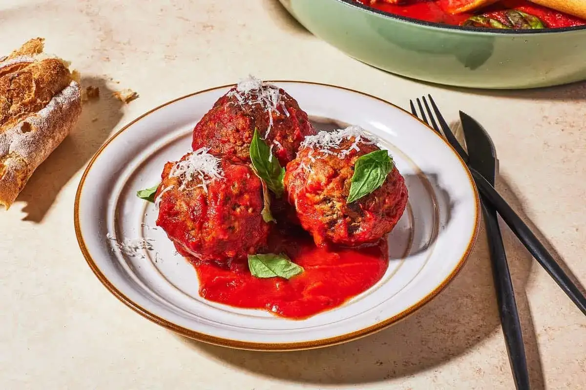 Drei saftige polpetta in Tomatensauce, garniert mit Parmesan und Basilikum, neben knusprigem Brot.