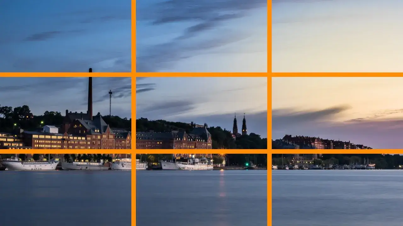 Paysage urbain au crépuscule, avec des bâtiments historiques et des bateaux le long de l'eau. Une grille de composition aide à s'améliorer en photographie.