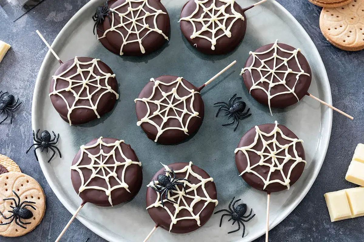 Délicieux **dessert Halloween** : des biscuits enrobés de chocolat noir, décorés de toiles d'araignées blanches et ornés d'araignées en plastique.