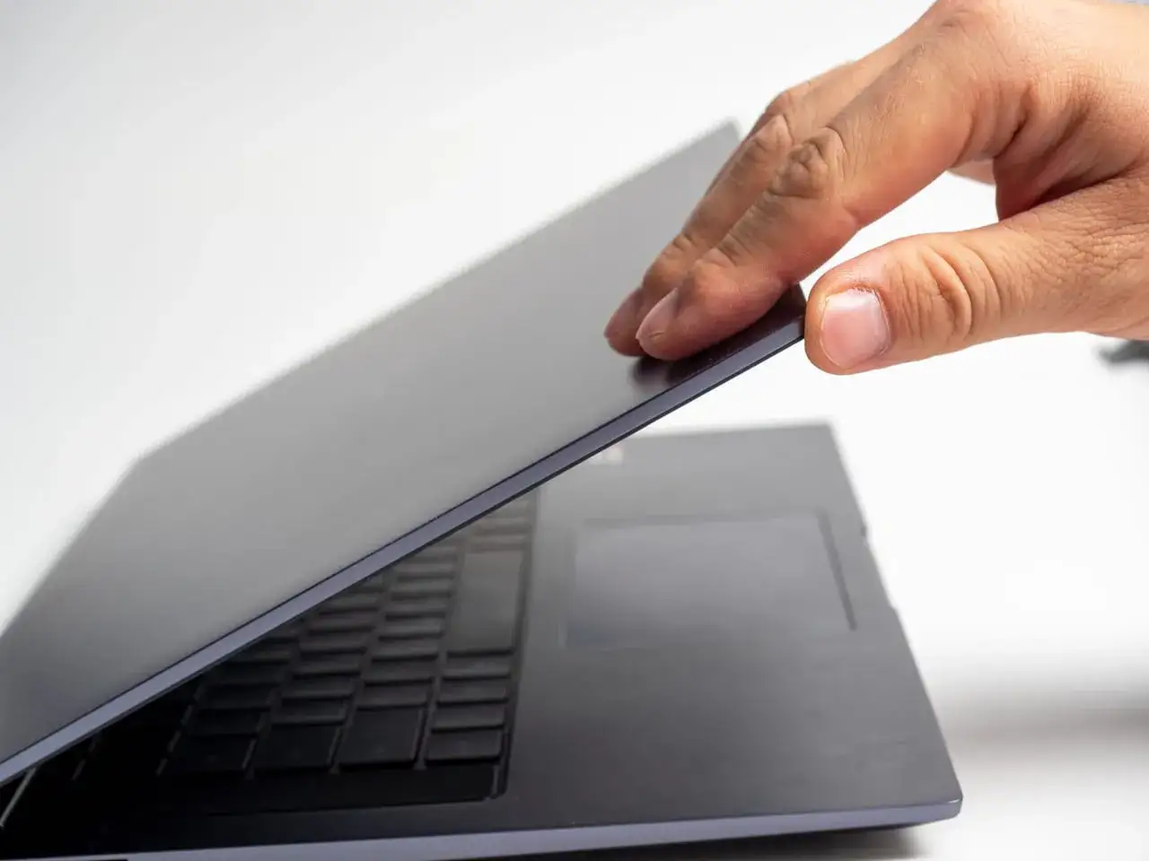 Dłoń zamyka ciemny laptop. Chcesz wiedzieć, jak sprawdzić ile cali ma laptop? To proste, wystarczy zmierzyć przekątną ekranu.
