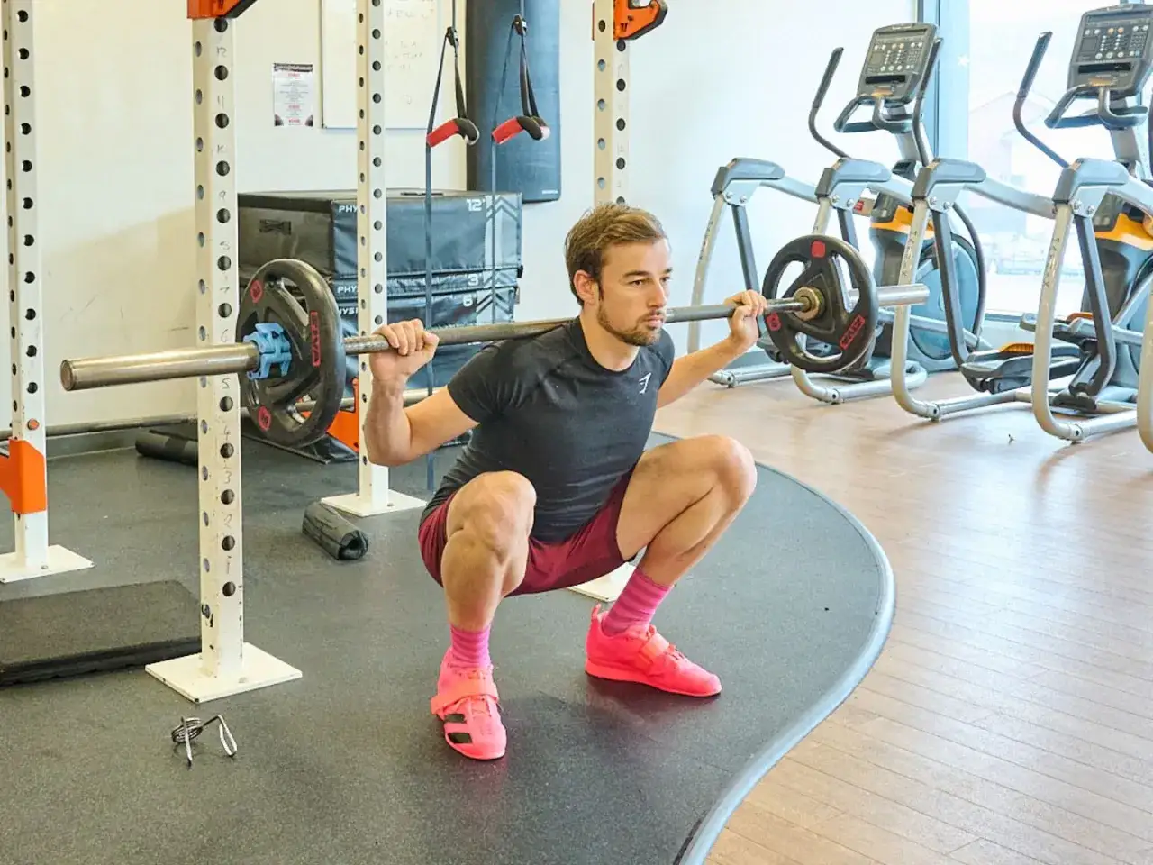 Mann mit schmaler Taille macht Kniebeugen mit Langhantel im Fitnessstudio.