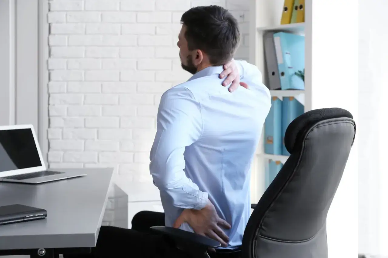 Mann im Büro mit schmerzen beim sitzen, hält sich den Rücken und Nacken.
