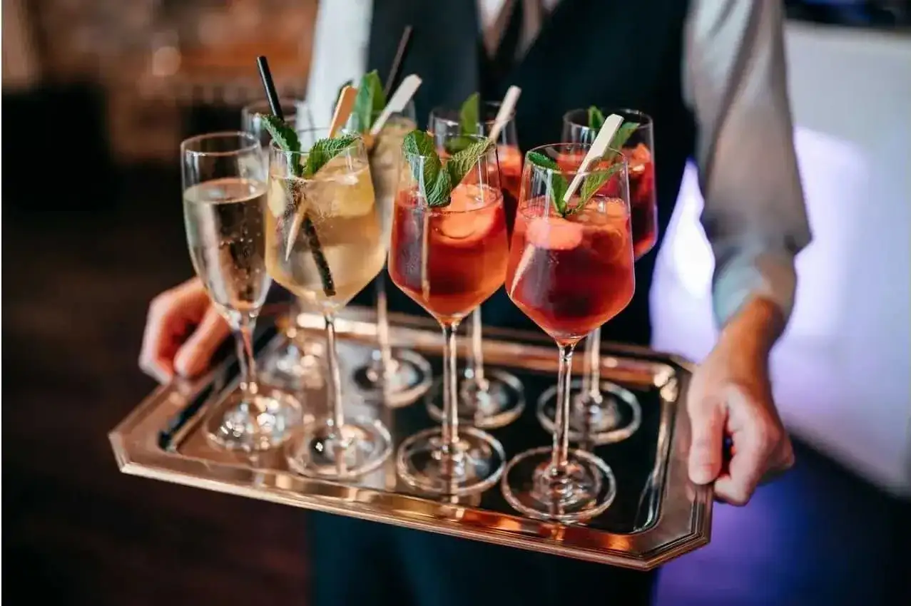 Un serveur porte un plateau argenté rempli de verres de **soupe de champagne** et de cocktails fruités, décorés de menthe fraîche.
