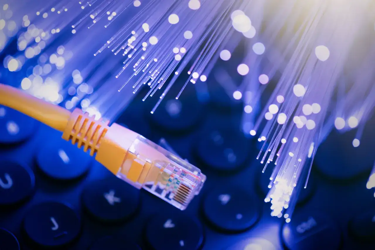 Żółty kabel sieciowy na klawiaturze, otoczony przez świecące światłowody symbolizujące szybki internet po kablu koncentrycznym.