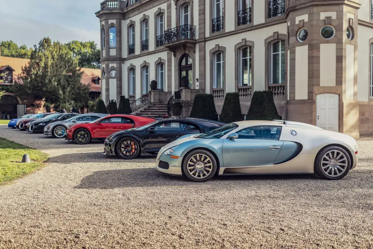Mehrere Bugatti-Supersportwagen stehen vor einem Herrenhaus. Wo kommt Bugatti her? Aus Frankreich, dem Land der Eleganz und des Luxus.