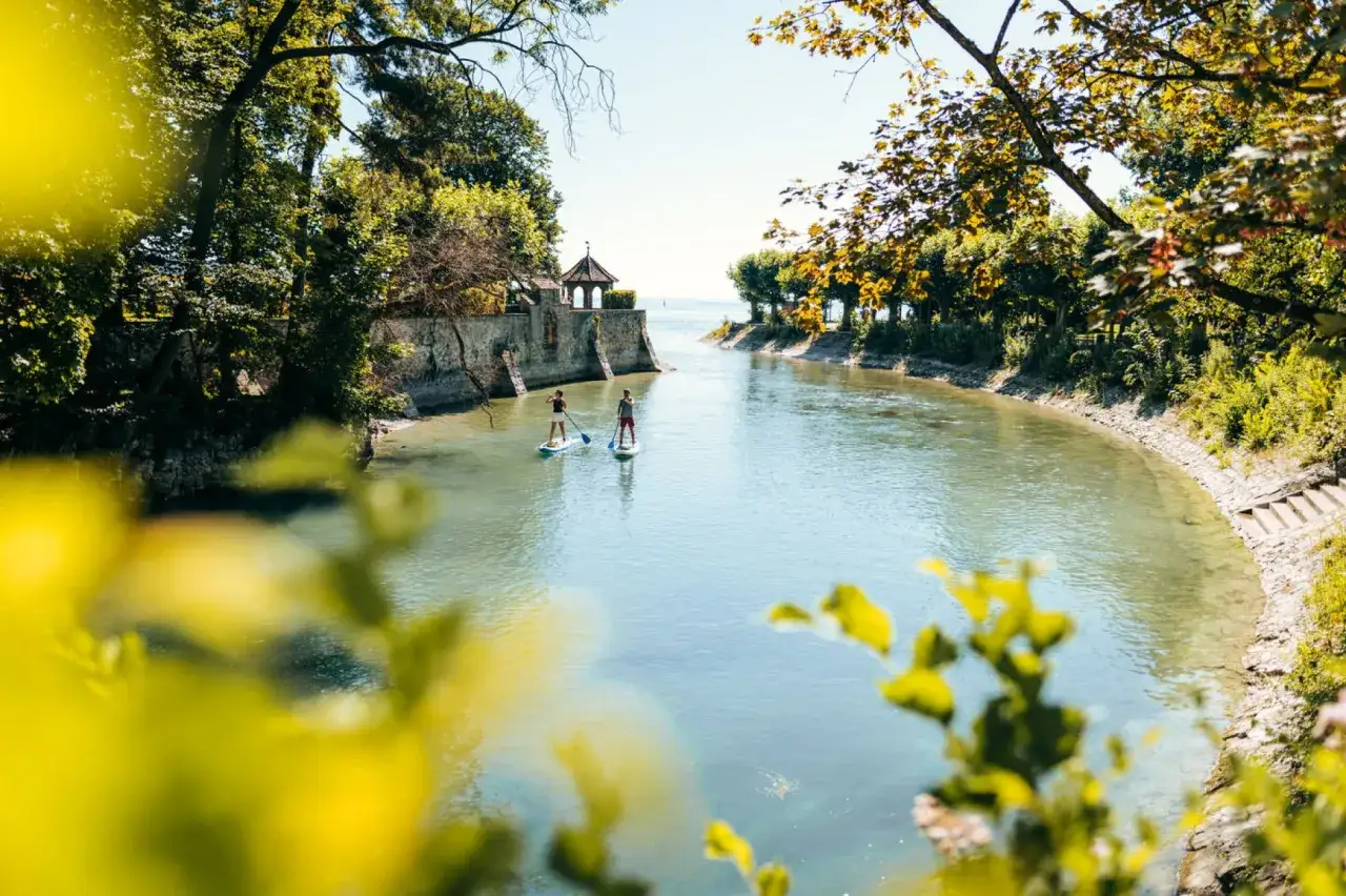 Zwei Personen auf SUP-Boards auf einem Fluss bei Konstanz. Ein idyllischer Ort f&uuml;r Sommeraktivit&auml;ten und Konstanz Events.