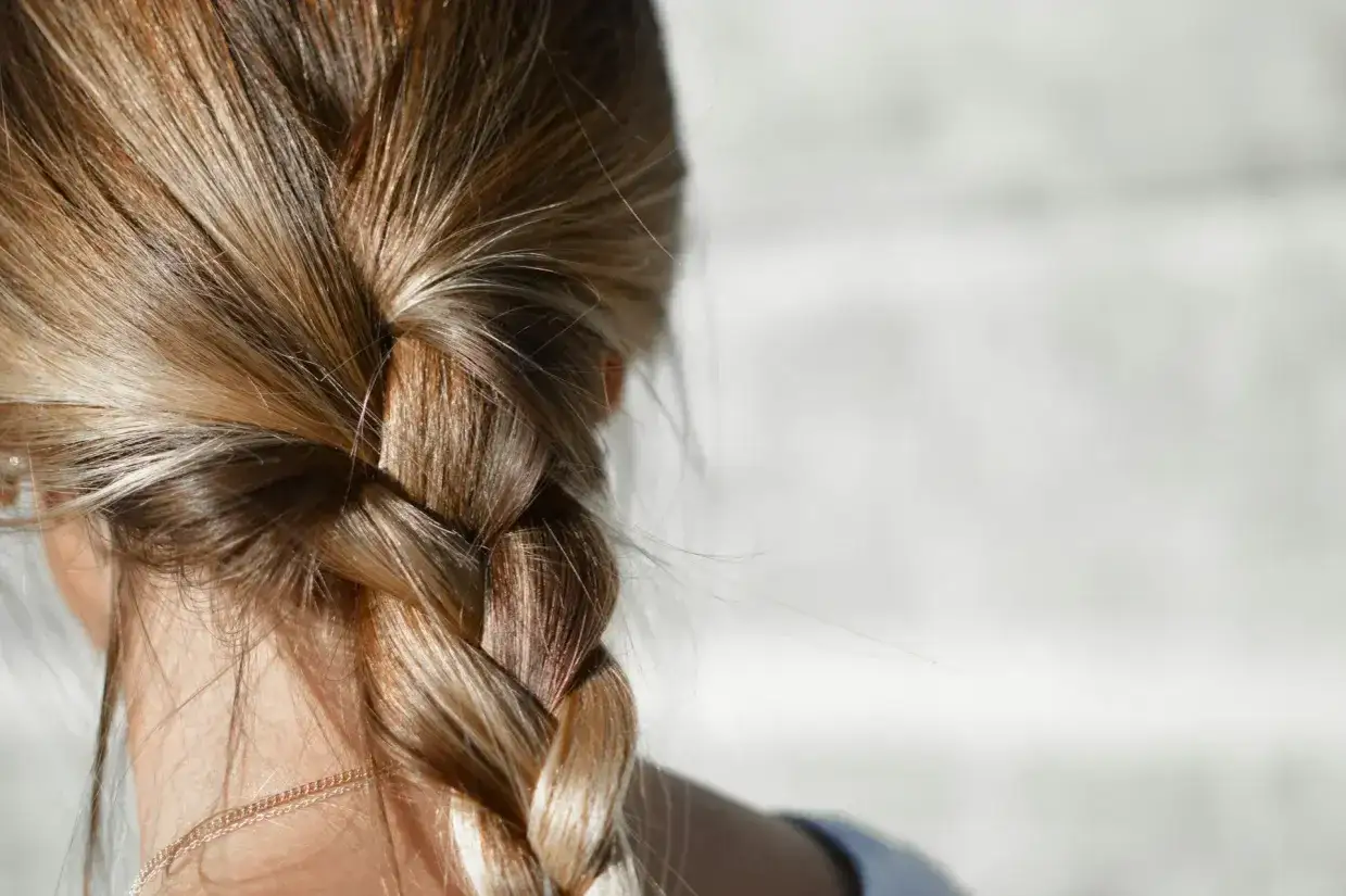 Capelli biondi intrecciati in una treccia, con qualche ciocca che sfugge, che suggerisce capelli unti dopo qualche giorno.