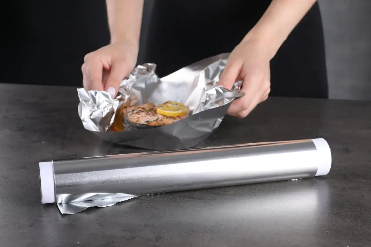 Préparation d'un saumon au citron dans du alu four. Les mains ajustent le papier d'aluminium autour du poisson.