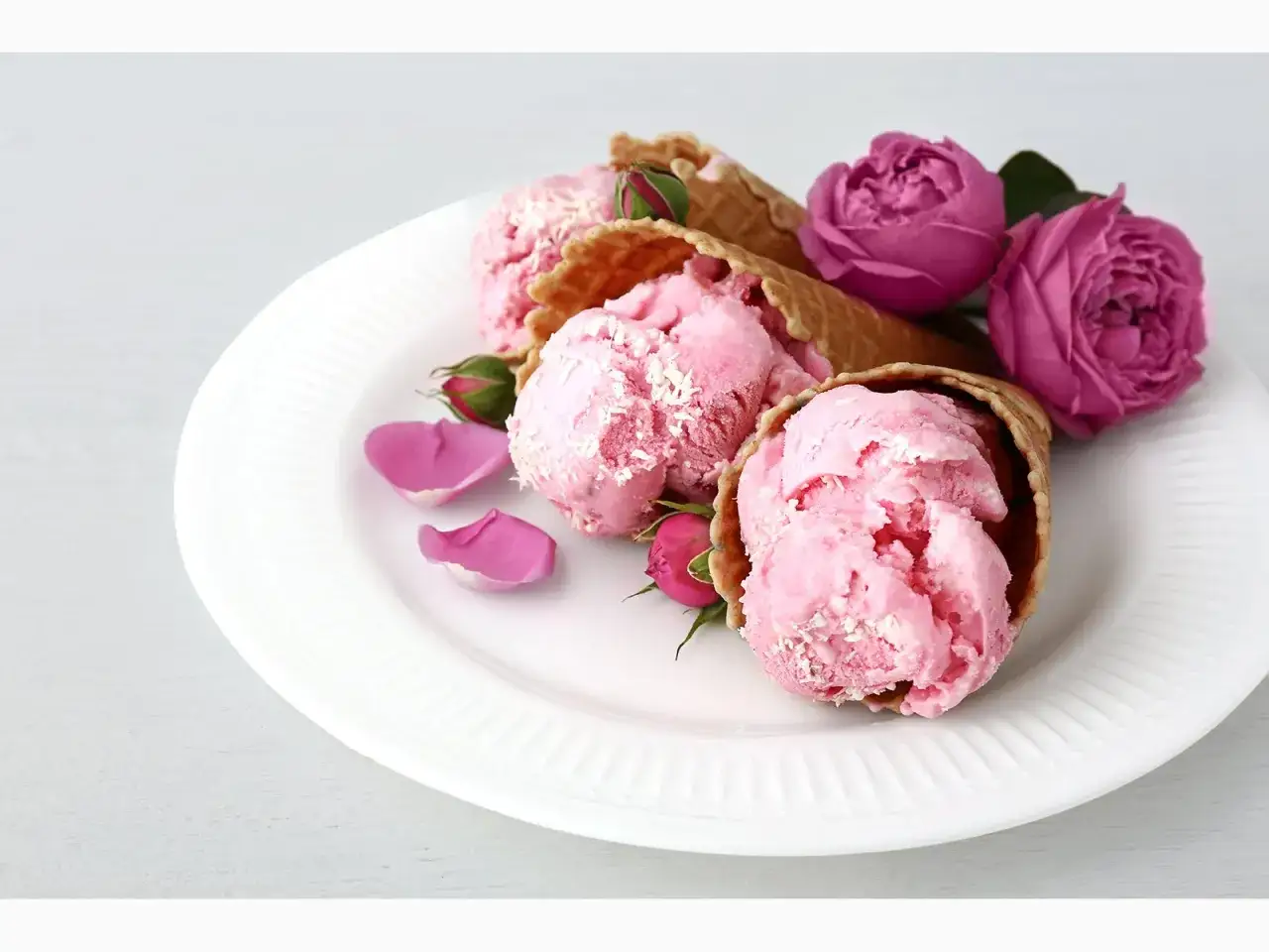 Zartes **Rosen-Eis** in Waffeln, dekoriert mit echten Rosenblüten und Blättern auf einem weißen Teller.