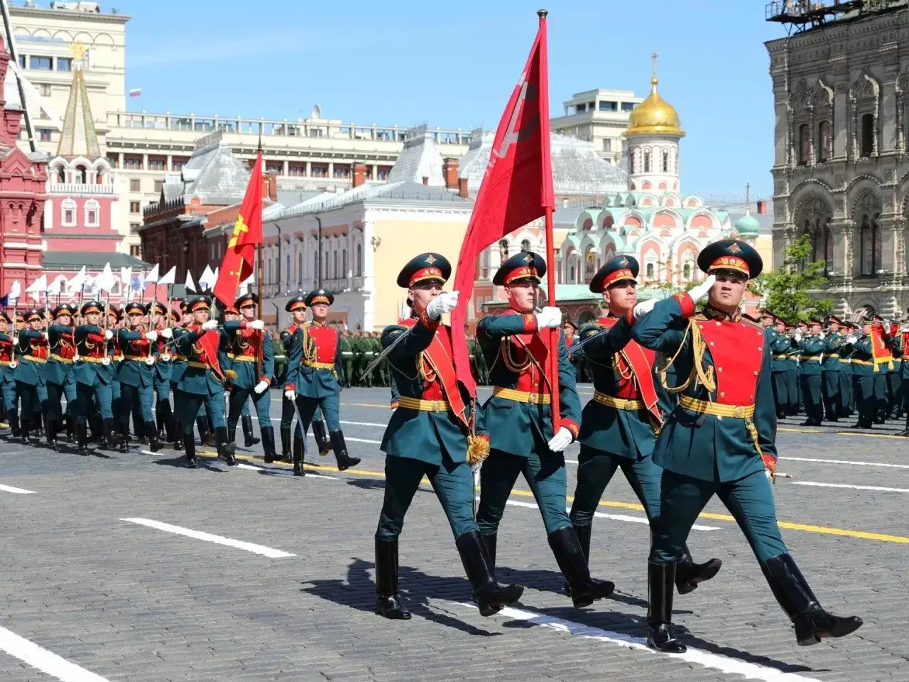 Uroczysta defilada wojskowa z okazji 9 maja. Żołnierze w historycznych mundurach maszerują z flagami na Placu Czerwonym.