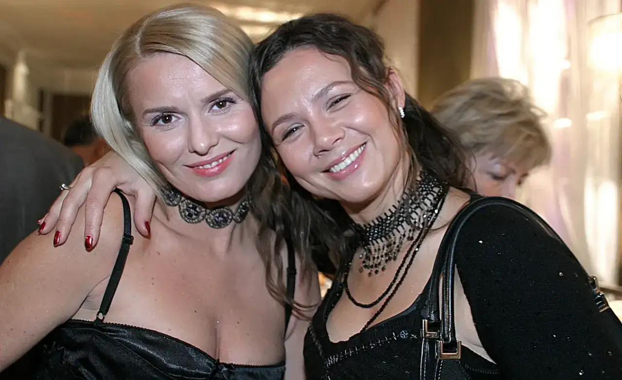 Hanna Lis i Kinga Rusin uśmiechają się do zdjęcia, obie w eleganckich czarnych kreacjach i ozdobnych naszyjnikach.