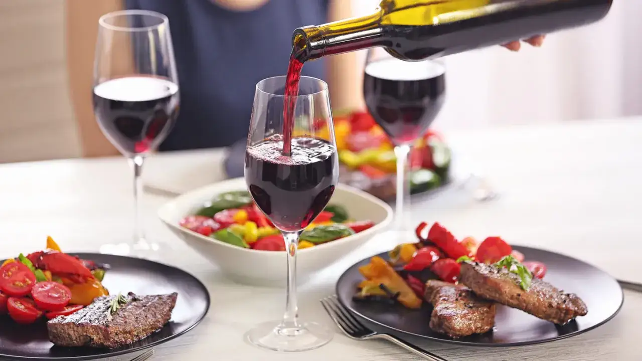 Servicio de vino tinto en copas, acompa&ntilde;ando un delicioso maridaje de vinos con filetes y ensalada de pimientos y tomates.