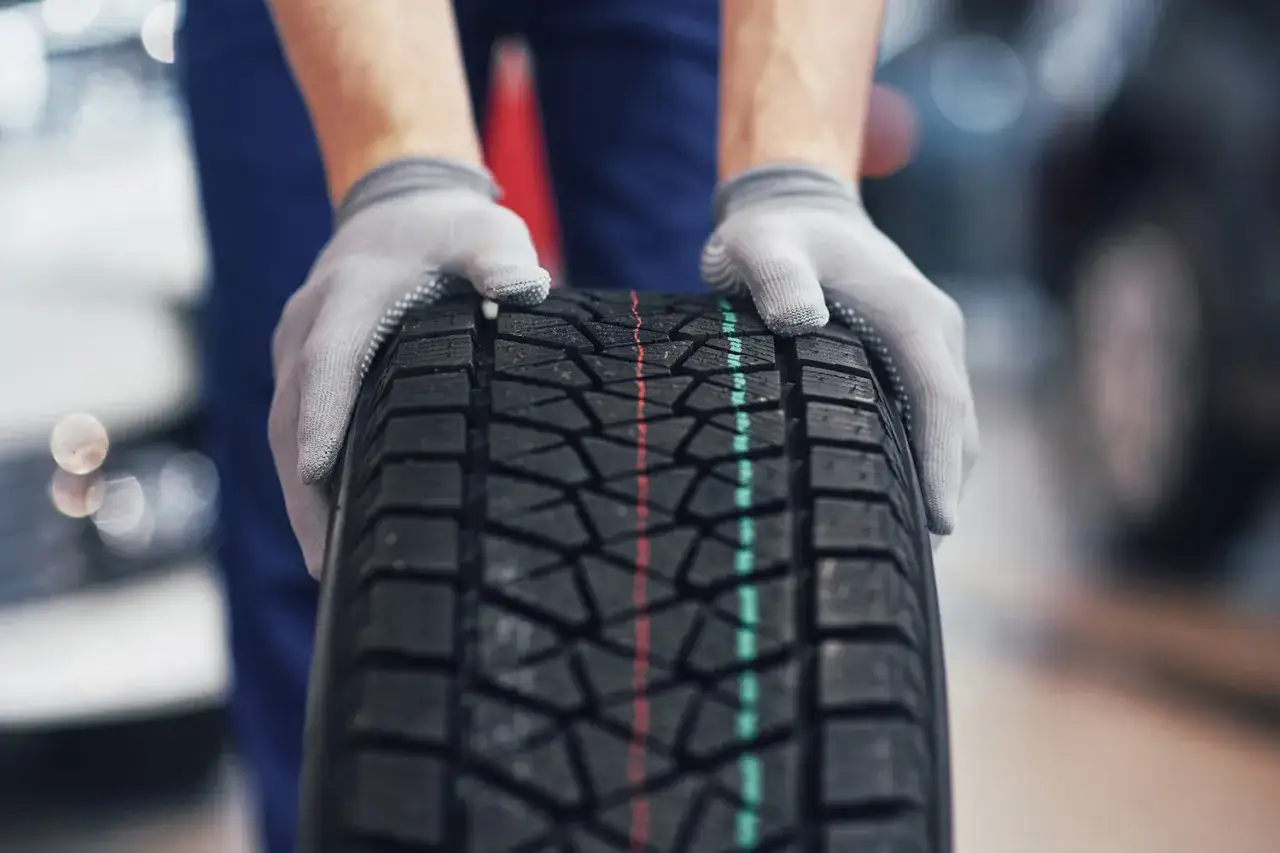 Mani guantate tengono un nuovo pneumatico, pronto per affrontare la neve. Gomme invernali neve per la tua sicurezza.