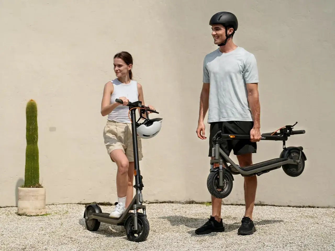 Un homme porte une trottinette Xiaomi pliée, tandis qu'une femme se tient à côté d'une autre, prête à rouler. Le poids de la trottinette Xiaomi est un facteur clé pour le transport.